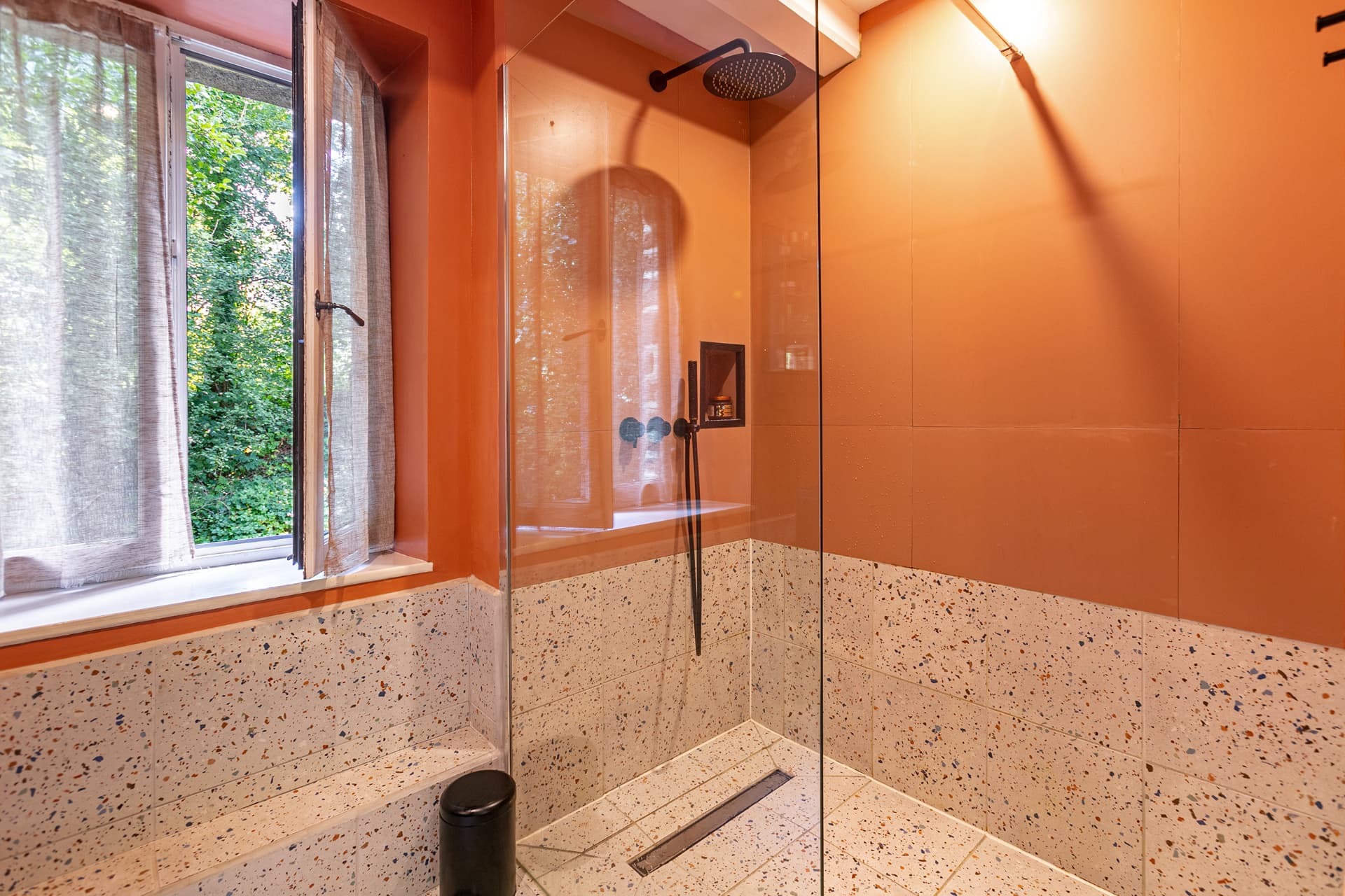 Walk-in rain shower beside a window onto greenery