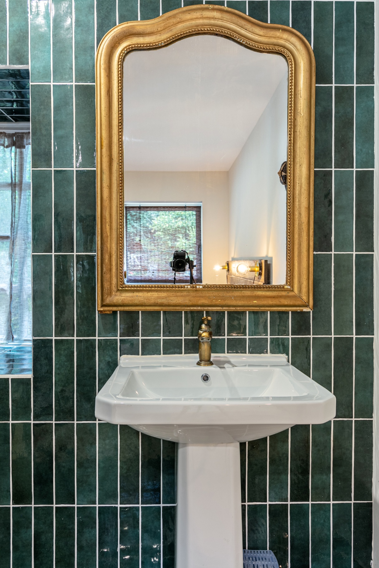 Gilded mirror above a pedestal basin on green tiles