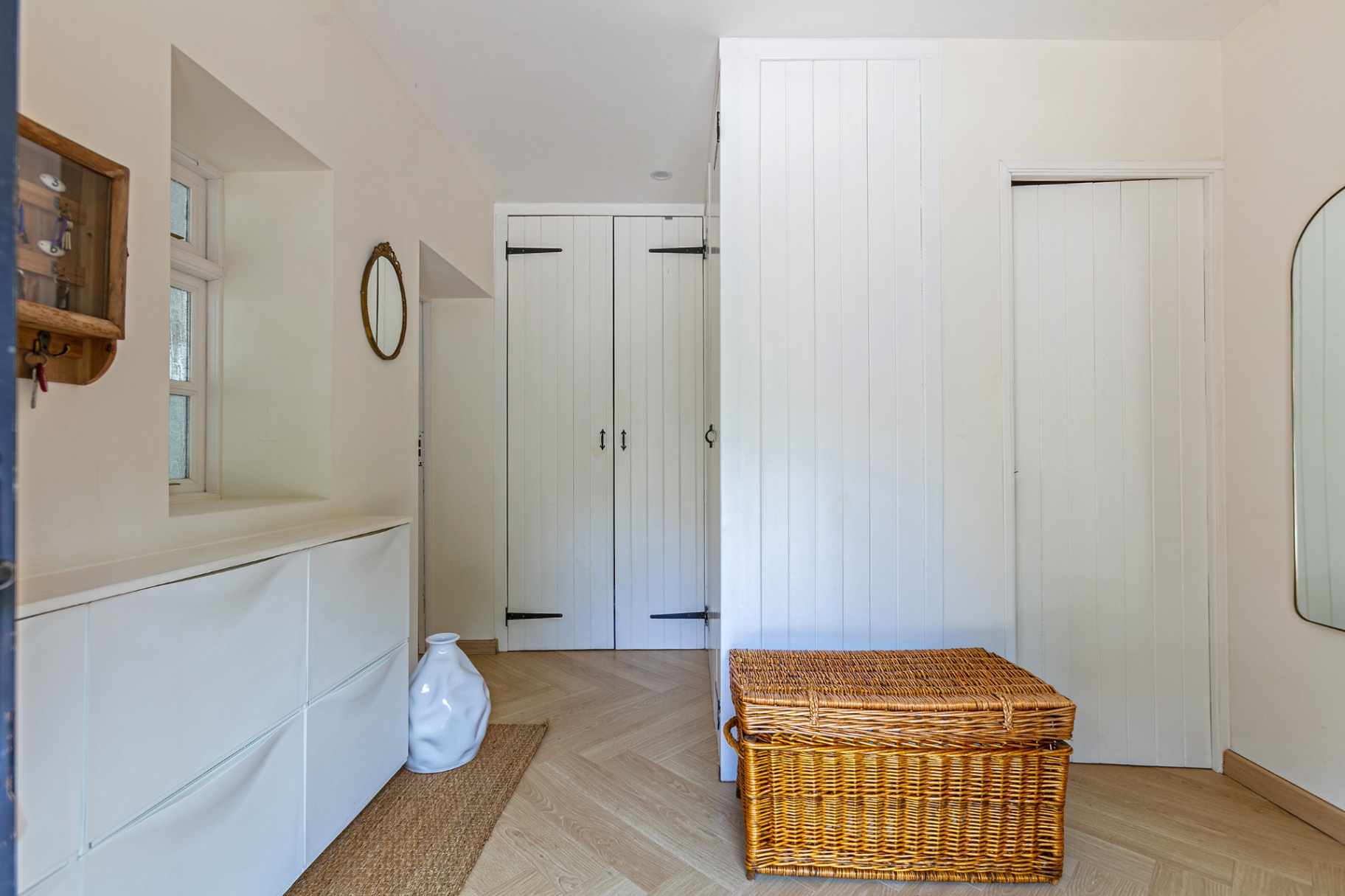 Bright hallway with wicker trunk, herringbone floor and plank doors