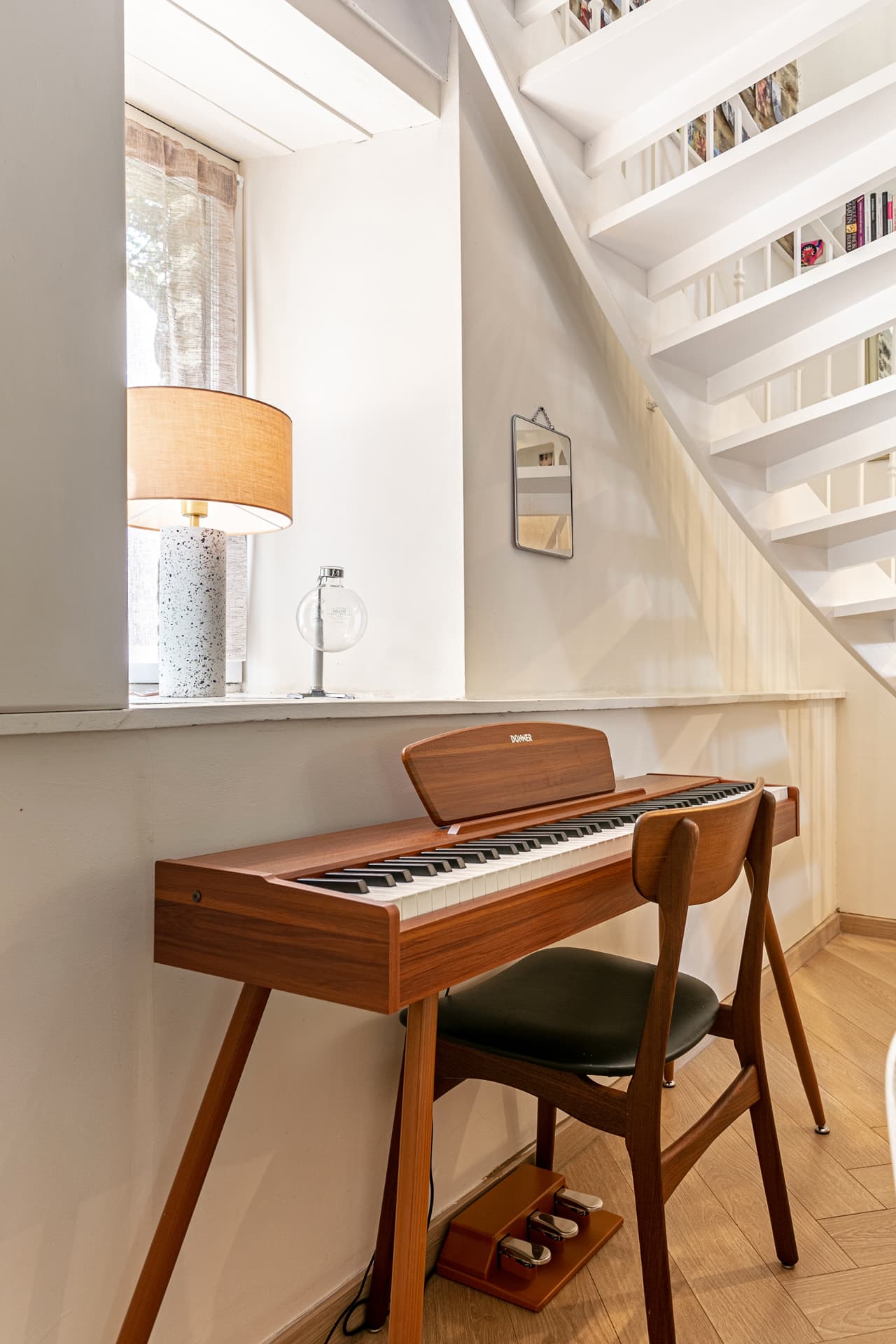 Wooden piano under the staircase beside a window