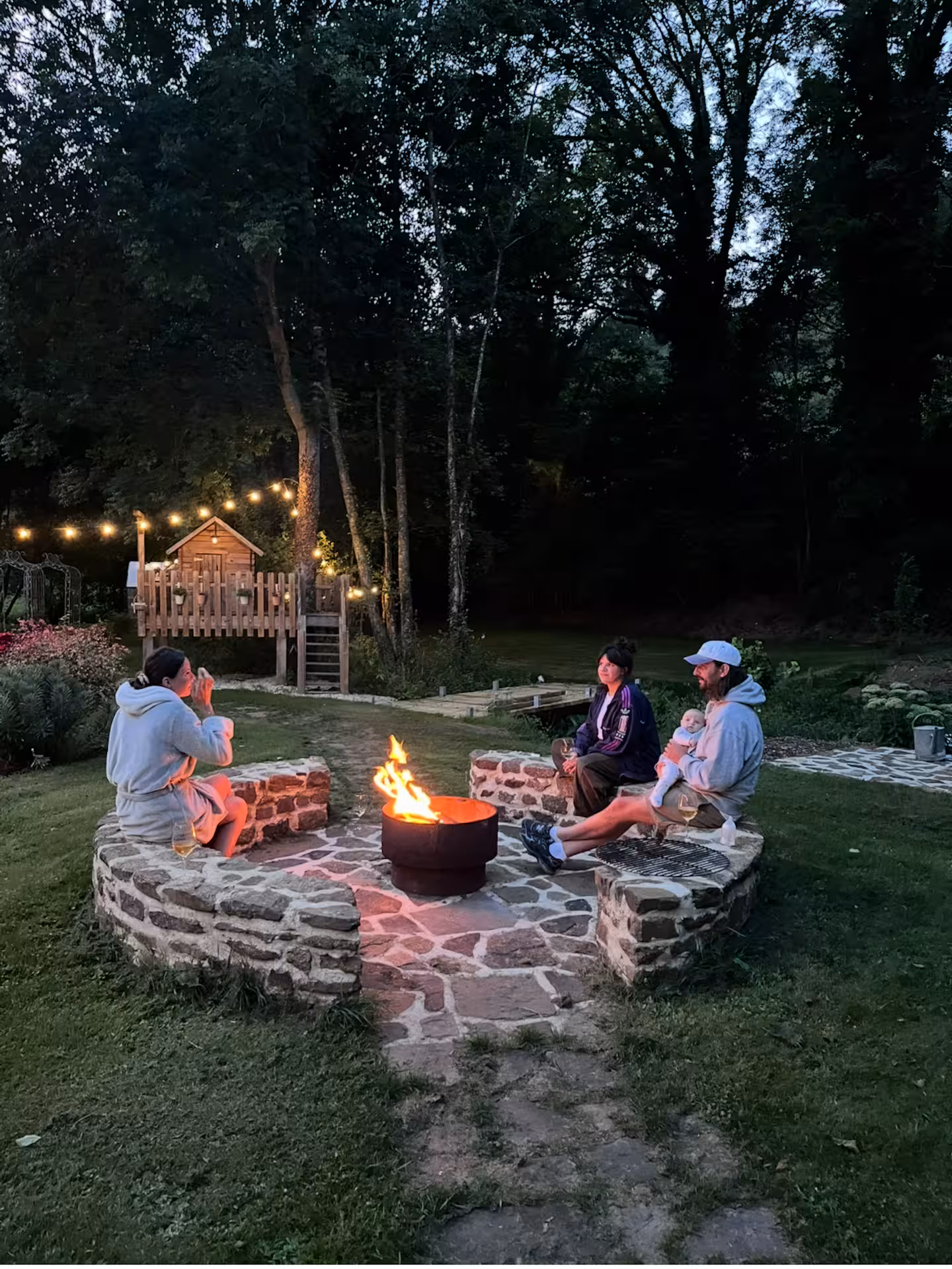 Guests sitting around the fire pit at dusk with lights in the trees