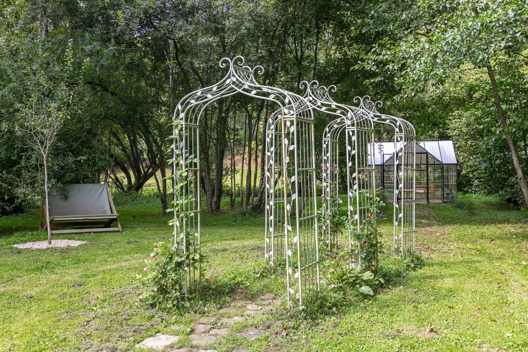 White rose arches across the lawn leading to the greenhouse