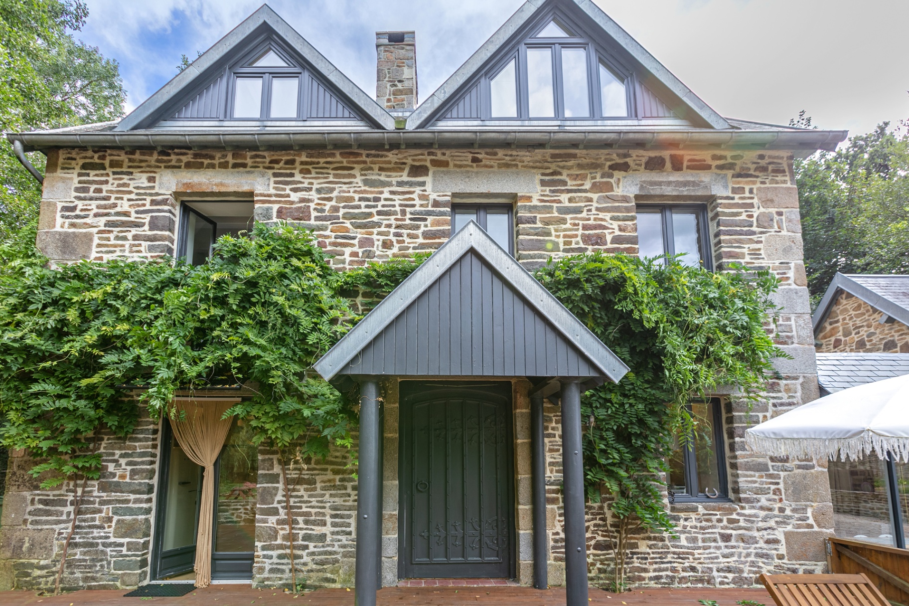 Stone house front with wisteria and slate gables