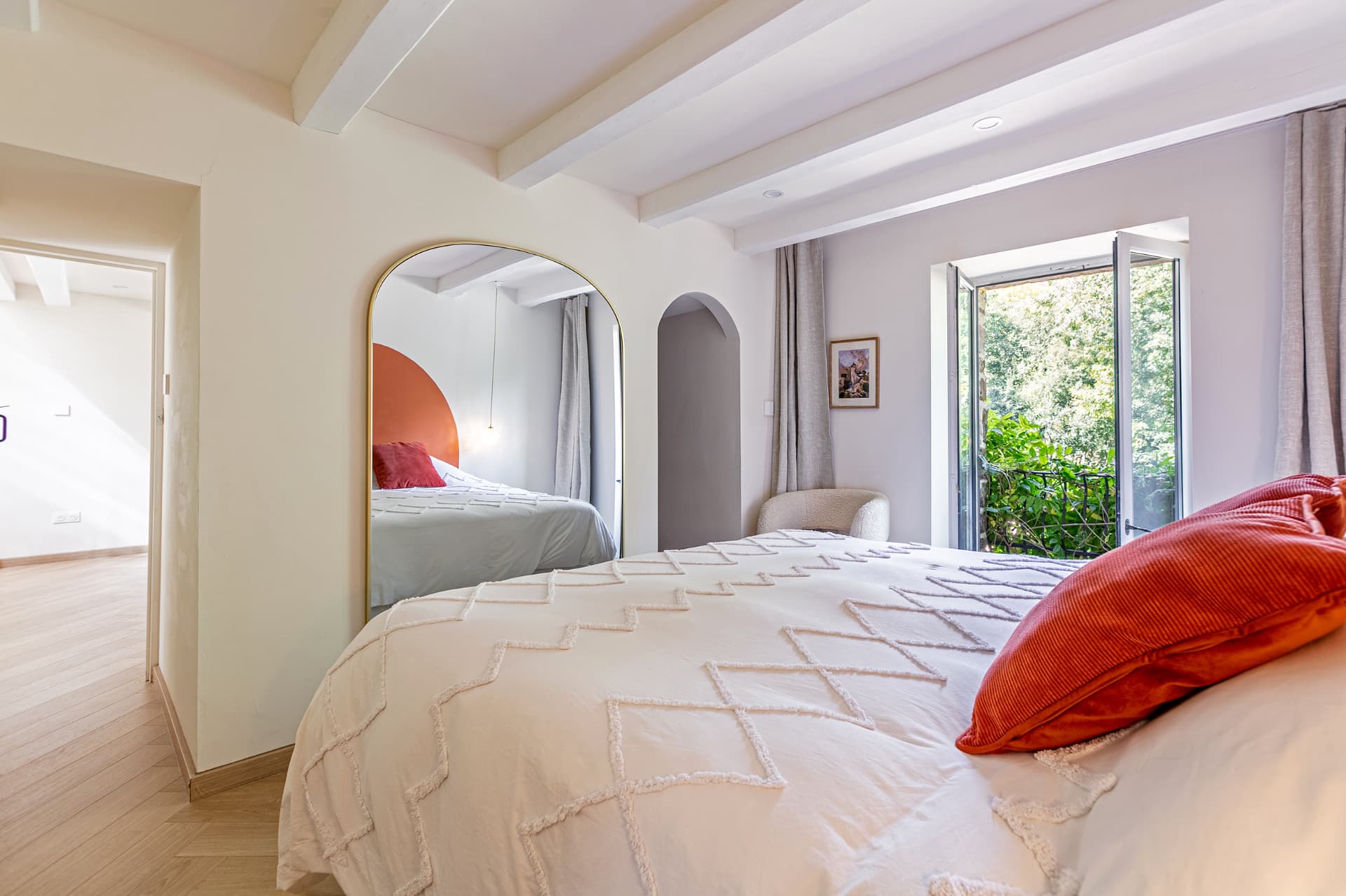 Bedroom with arched mirror and open window to the trees