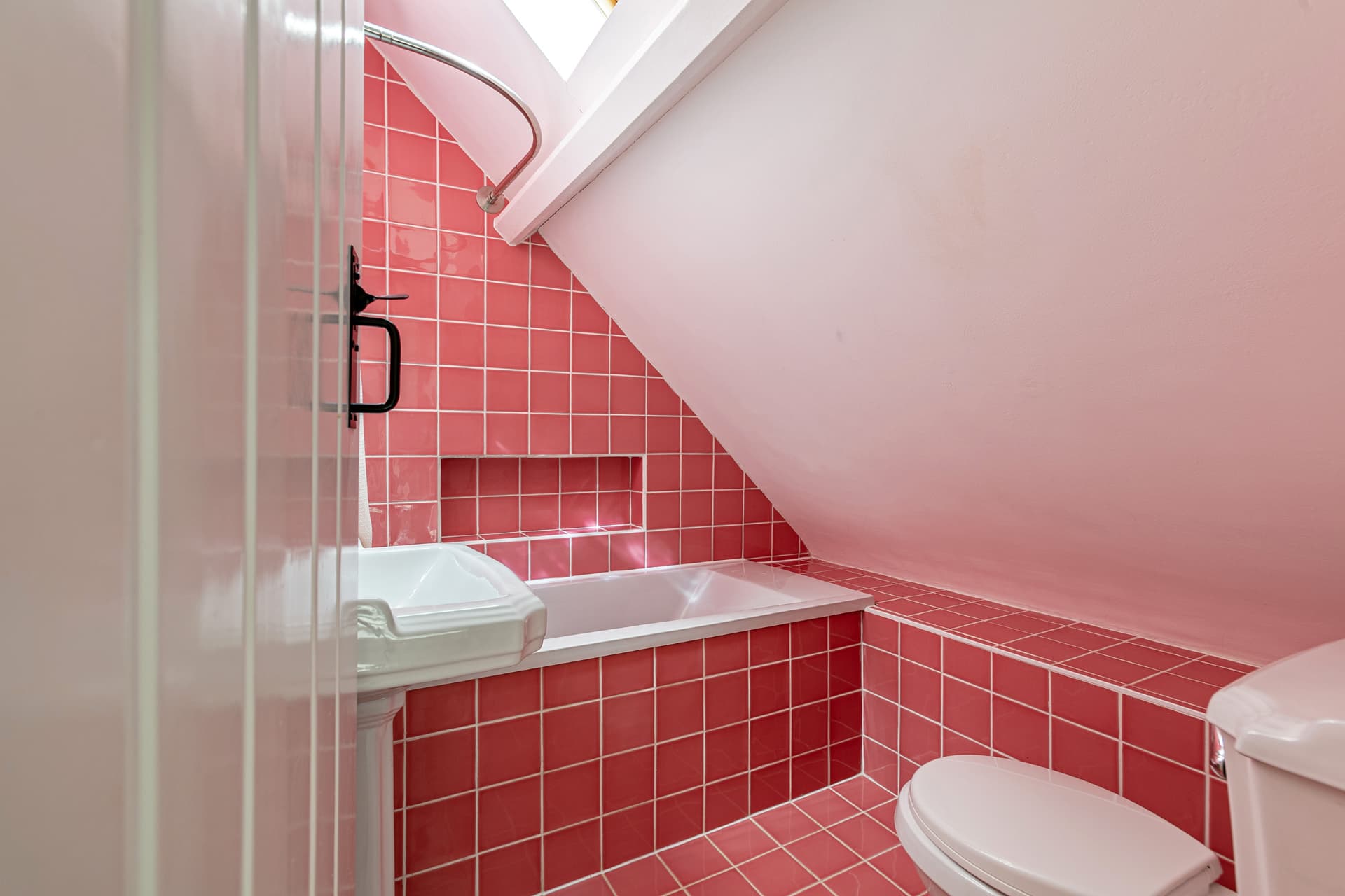 Pink-tiled bathroom with bath under a sloping ceiling